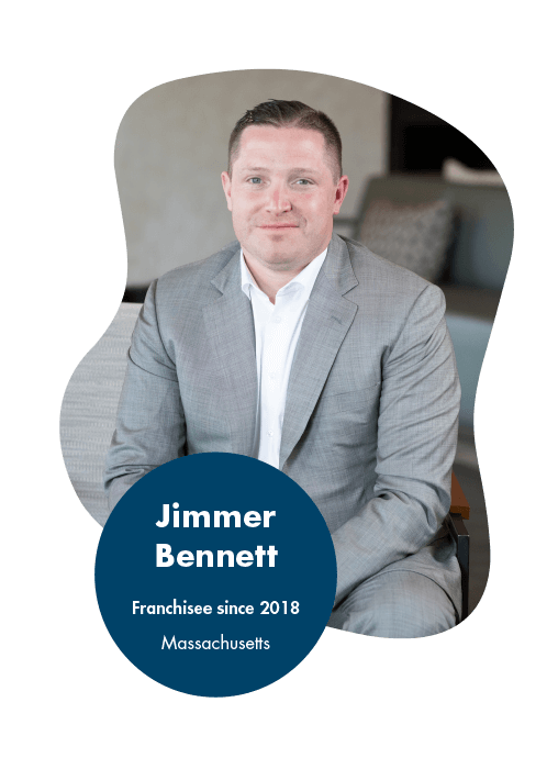 Jimmer Bennett - Logistics Franchise Opportunity Reviews and Testimonials A person in a gray suit sits on a chair, looking at the camera. Text overlay reads: Jimmer Bennett, Franchisee since 2018, Massachusetts. His franchise journey mirrors the positive franchise reviews by owners, showcasing dedication and success.