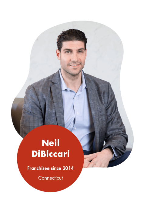 Neil DiBiccari - Logistics Franchise Opportunity Reviews and Testimonials A person wearing a gray plaid blazer and light blue shirt sits on a chair. A red circular caption overlay reads Neil DiBiccari, Franchisee since 2014, Connecticut, known for positive franchise reviews by owners.
