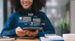 A person, embodying the spirit of happy customers, smiles while using a tablet at a desk. Floating icons display five-star ratings and positive testimonials. A potted plant and a calculator add charm to the scene.