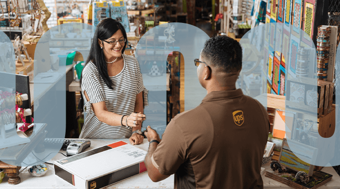 A smiling woman hands a payment card to a UPS employee across a counter, with a cardboard package in front of them at a colorful, busy logistics shop.
