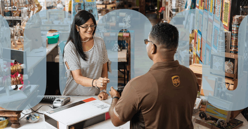 A woman smiles as she hands a card to a UPS employee at a store counter with a large package on the desk, surrounded by colorful items and shelves.
