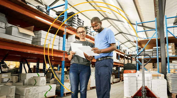 Two people stand in a warehouse, reviewing documents together. Shelves filled with boxes and supplies surround them, and yellow graphics form a partial circle around the pair, highlighting their collaboration.
