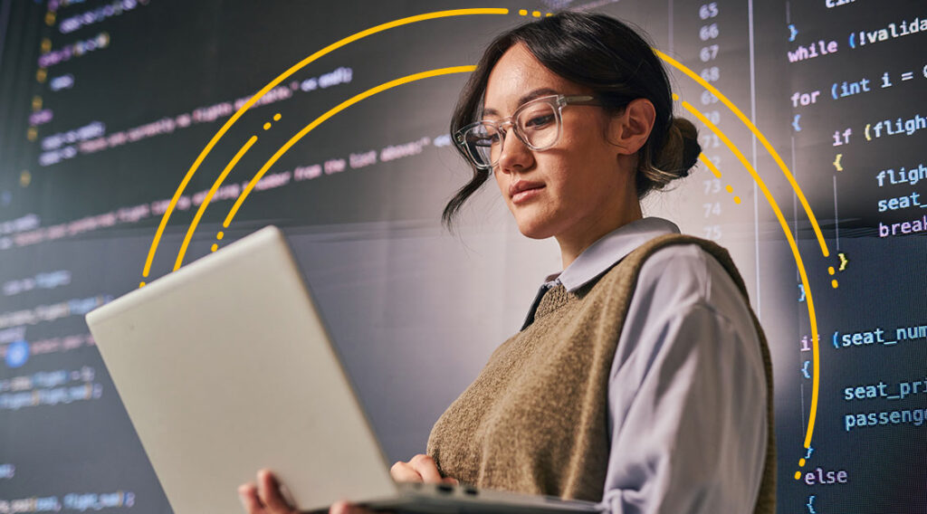 A person with glasses uses a laptop, with programming code and yellow curved lines—hinting at transportation technology—displayed on a screen in the background.